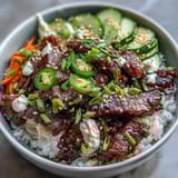 Freshly seared sesame-ginger beef layered over steamed rice, topped with tangy pickled carrots and crisp cucumber slices.