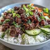 Korean Beef Bowl with pickled vegetables, steamed rice, and spicy gochujang beef, garnished with sesame seeds and fresh cucumber slices.  