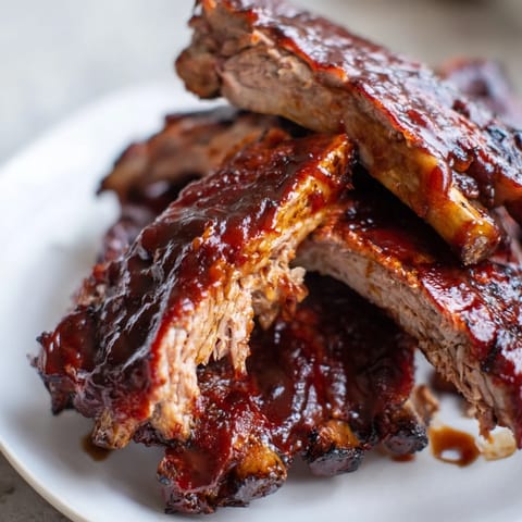 Slow-cooked BBQ Ribs glazed with smoky barbecue sauce, resting on a platter ready for sharing.