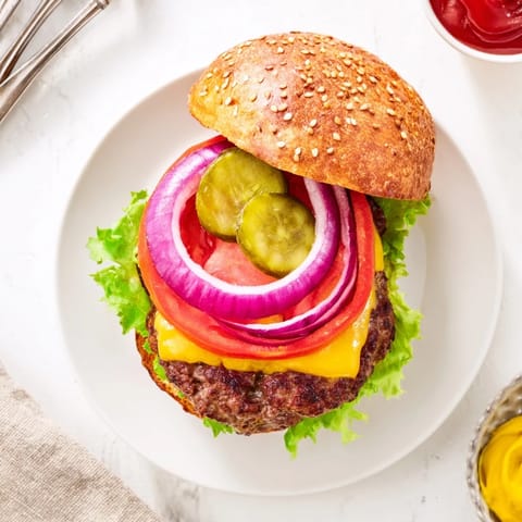 Golden brown hamburgers on soft buns topped with lettuce tomato onion pickles and condiments.