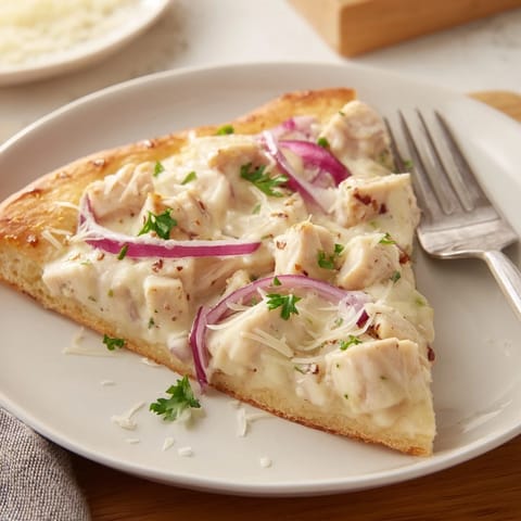 A close-up slice of Chicken Alfredo Pizza revealing tender chicken and bubbly cheese topping.  