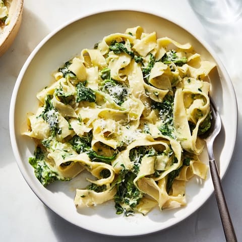 Plate of creamy spinach garlic noodles twirled on a fork, with a sprinkle of Parmesan and a glass of white wine nearby.