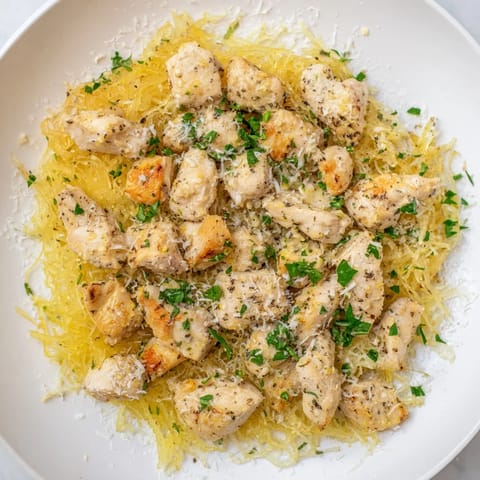 Fork-tender spaghetti squash serves as a gluten-free base for juicy lemon garlic chicken, finished with Parmesan and fresh herbs.