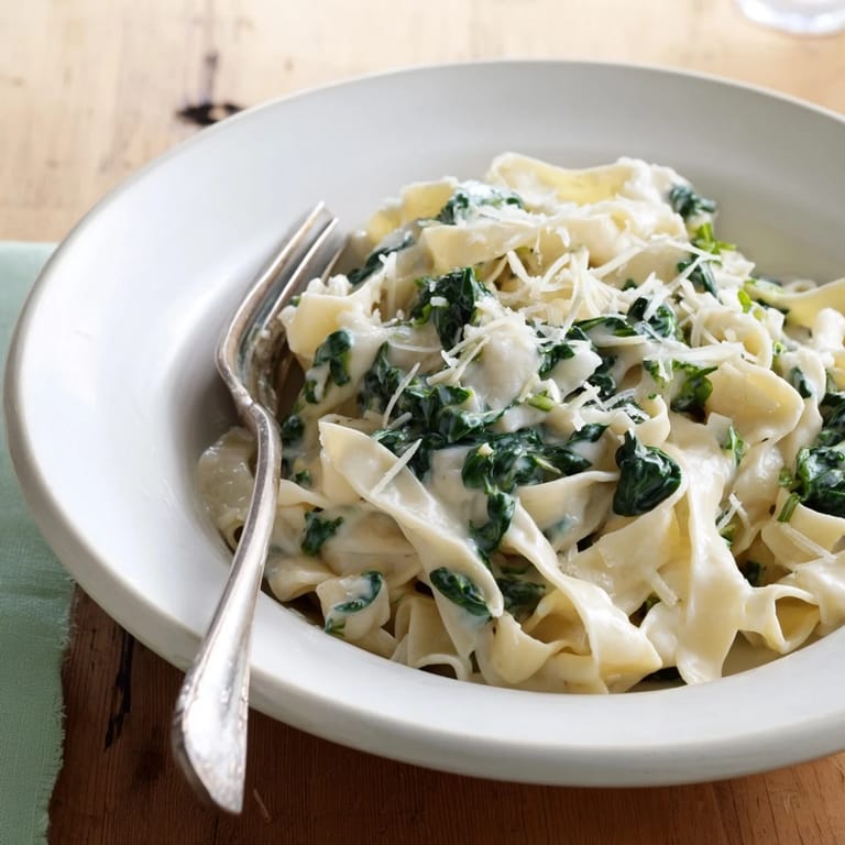 Overhead view of creamy spinach garlic noodles in a ceramic bowl, garnished with fresh parsley and a dash of red pepper flakes.