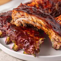 Glossy, fall-off-the-bone BBQ Ribs coated in sticky barbecue sauce, served with cornbread and slaw.